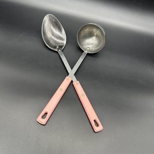 Puede incluir: Dos utensilios de cocina con mangos rosas. Uno es una cuchara ranurada y el otro es un cucharón.