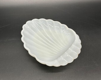 Puede incluir: Un plato de cerámica blanca con forma de concha. El plato tiene un acabado liso y brillante y una textura ligeramente ondulada.
