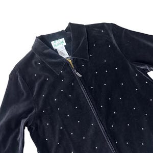 May include: Black velvet zip-up jacket with a collar and scattered white rhinestone embellishments. The jacket has a zipper with a rhinestone pull and a tag with a green logo.
