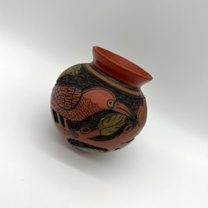 May include: A small, round, terracotta pot with a red glaze and black and brown painted designs of birds and leaves.