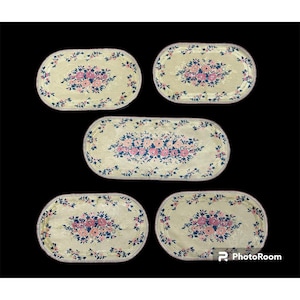 Könnte beinhalten: Fünf ovale Tischsets mit floralem Design. Die Tischsets haben einen cremefarbenen Hintergrund mit einem rosa-blauen Blumenmuster in der Mitte. Die Ränder sind mit einer dekorativen Bordüre versehen.