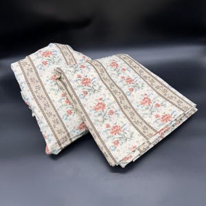May include: Two folded fabric panels featuring a cream background with vertical beige stripes and a repeating floral pattern of orange-red blossoms and green leaves. The textile has a soft, matte texture and is arranged in overlapping layers.