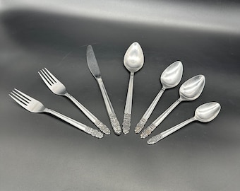 May include: A set of six silver-toned flatware pieces, including two forks, a knife, and three spoons. The handles of the flatware are decorated with an ornate floral design.