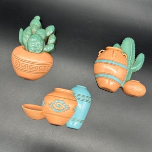 May include: Set of four ceramic wall decor pieces in southwestern style. The set includes a cactus with a pot, a pot with a cactus design, a pot with a geometric design, and a pot with a blue and white design.