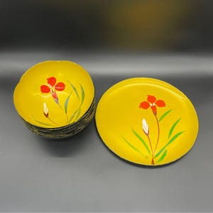 May include: A set of yellow lacquerware consisting of a stack of bowls and a single matching plate. Each piece features a hand-painted design of a vibrant red iris flower with green leaves and a white bud centered on the bright yellow surface.