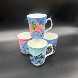May include: Set of four ceramic mugs with whimsical animal illustrations. Each mug features a different animal, including a pig with wings, a monkey, and two cats. The mugs are painted in a blue and pink color scheme.