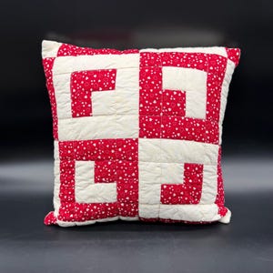 May include: A square throw pillow featuring a patchwork quilt design. The fabric alternates between solid off-white squares and red squares patterned with small white hearts, arranged in a repeating geometric pattern across the entire surface.