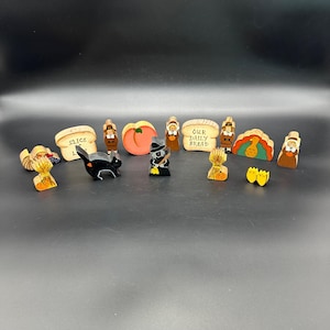 May include: A collection of wooden figurines and signs with a Thanksgiving theme. The figurines include a witch, pilgrims, a turkey, and a black cat. The signs include "Our Daily Bread" and "Slices of..."