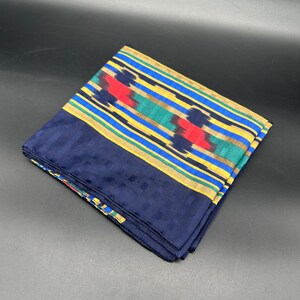 May include: Folded navy blue scarf with a patterned border. The border features a design of red, green, and yellow stripes. The scarf has a textured appearance and is folded neatly.