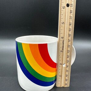 May include: White ceramic mug with a rainbow design. The rainbow is made up of red, orange, yellow, green, blue, and purple stripes. The mug is about 4 inches tall.