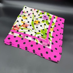 May include: A square scarf featuring a white background with a black polka dot pattern and a vibrant floral print of pink, yellow, and purple flowers. The scarf is bordered by a wide, bright pink band with black polka dots along the edges.