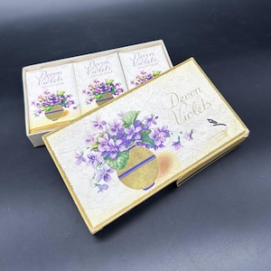 May include: A box of Devon Violets toilet soap. The box and individual soap wrappers feature a floral design of purple violets in a gold vase. The box is cream-colored with gold trim and the words "Devon Violets" are printed on the box.