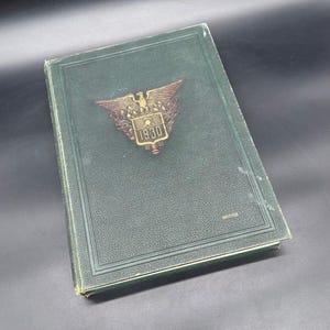 Peut inclure: Un livre vert vintage à couverture rigide avec une couverture texturée. La couverture présente un emblème de couleur bronze avec un aigle et l'année "1930". Le livre est de forme rectangulaire et semble en bon état.