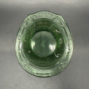 May include: A green glass bowl with a horseshoe shape and the words "Good Luck" embossed on the rim. The bowl has a circular base and a textured rim, perfect for serving snacks or as a decorative piece.