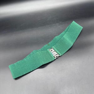 May include: A green ribbed elastic belt with a silver-tone clasp. The belt is a solid, vibrant green color and has a textured, ribbed design. The clasp has three interlocking rings.