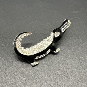 May include: A black enamel alligator brooch with rhinestones. The alligator is standing on its hind legs with its tail curled up.