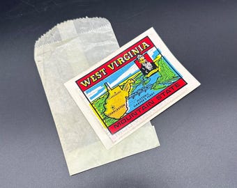 Könnte beinhalten: Ein Vintage-Aufkleber mit einer Karte von West Virginia mit dem Text "West Virginia Mountain State" und einem Porträt eines Mannes. Der Aufkleber befindet sich auf einem weißen Papierbeutel.