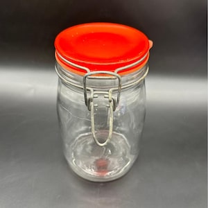以下が含まれることがあります： 鮮やかなオレンジ色のプラスチック製蓋と金属製のワイヤーベイルクロージャーを備えた透明なガラス製保存瓶。円筒形の容器は滑らかで透明な本体を持ち、蓋をしっかりと固定するための安全なラッチシステムが装備されています。
