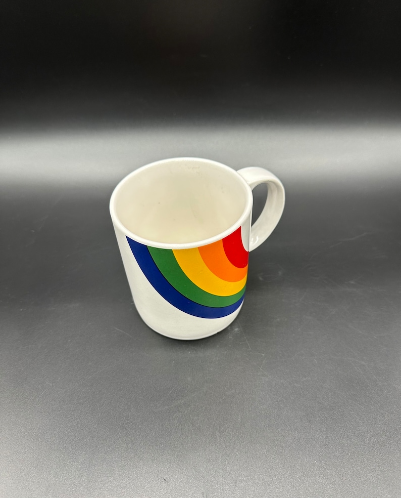 May include: White ceramic mug with a rainbow design. The rainbow is in a curved shape and the colors are red, orange, yellow, green, blue, and purple.