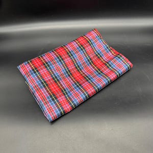 May include: Folded red, blue, black, and yellow plaid fabric. The fabric has a classic tartan pattern, with intersecting lines creating a grid-like design. The fabric is folded neatly, showcasing the pattern's symmetry and color arrangement.