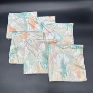 May include: A set of six square pillowcases with a pastel feather pattern in shades of white, peach, mint green, and lavender. The pillowcases are arranged in a layered display, showcasing the repeating design.