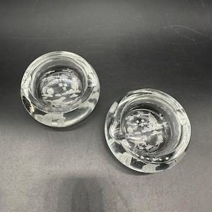 Puede incluir: Dos ceniceros de vidrio transparente con un borde elevado y un diseño grabado decorativo de nubes y pájaros.