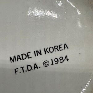 May include: Close-up of a white ceramic mug with black text that reads "MADE IN KOREA F.T.D.A. &copy; 1984".