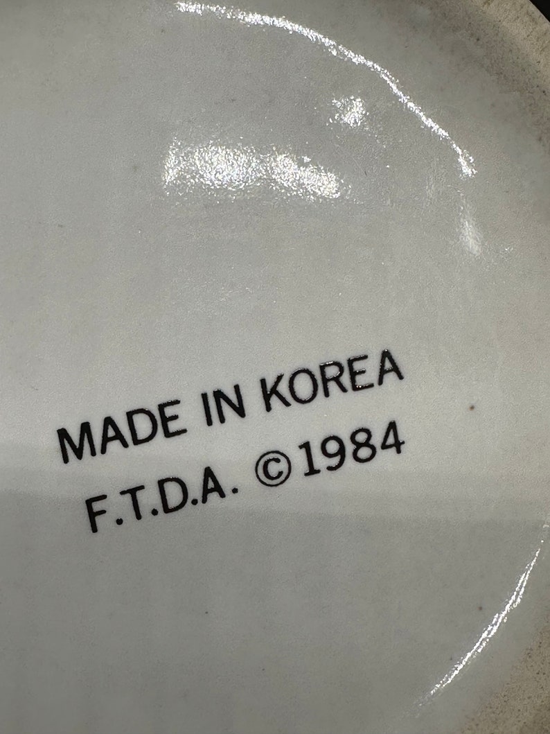 May include: Close-up of a white ceramic mug with black text that reads "MADE IN KOREA F.T.D.A. &copy; 1984".