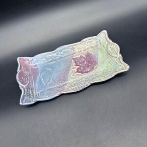 May include: A rectangular ceramic tray with a wavy edge. The tray features a leaf design in the center and on the corners. The colors include shades of blue, green, and purple. The tray is approximately 8 inches long.
