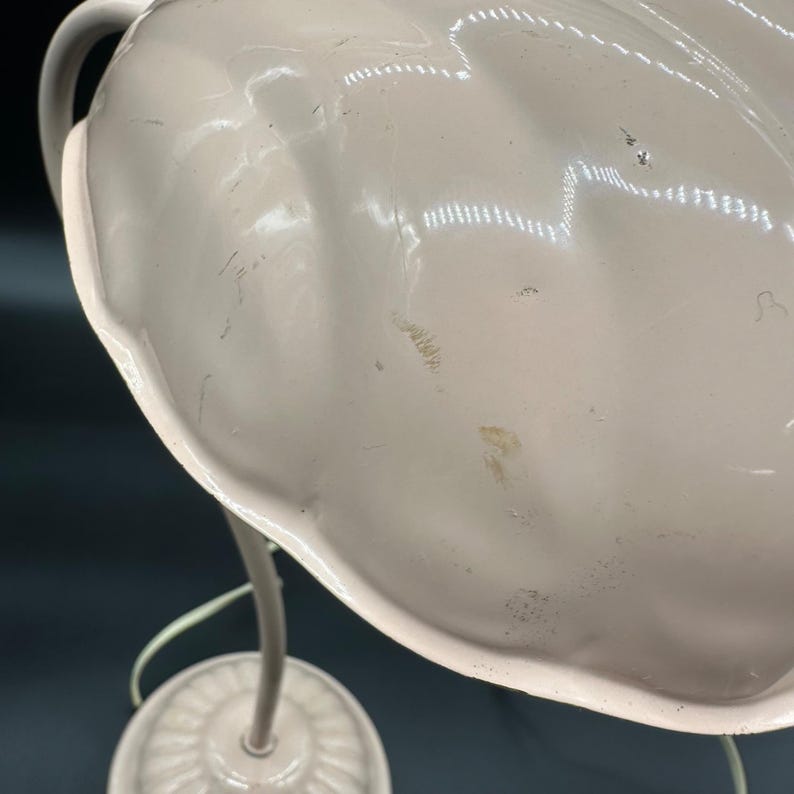 K&ouml;nnte beinhalten: Nahaufnahme einer Vintage-Lampe aus cremefarbenem Metall. Die Lampe hat einen gro&szlig;en, gewellten Schirm und einen gebogenen Stiel. Der Sockel ist rund mit einem dekorativen Muster. Die Lampe hat eine neutrale Farbpalette.