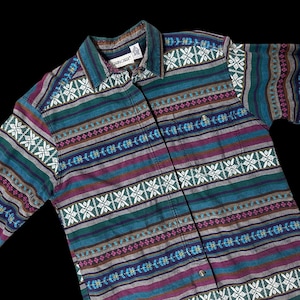 May include: A button-down shirt with a colorful geometric pattern. The shirt features horizontal stripes in teal, purple, brown, and gray, with white and teal geometric accents. The collar has a teal and purple striped pattern. The shirt is made of a soft, woven fabric.