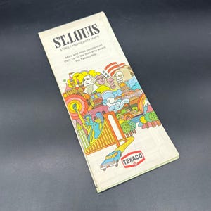 May include: Vintage St. Louis street and vicinity map. The cover features colorful illustrations of landmarks and a car driving on a yellow road. The Texaco logo is visible. The text reads "ST. LOUIS STREET AND VICINITY MAPS".