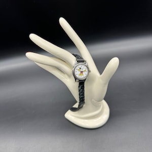 May include: A silver wristwatch with a white face and black Mickey Mouse character. The watch has a black braided leather band.