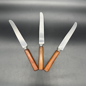May include: Three stainless steel butter knives with brown wooden handles.