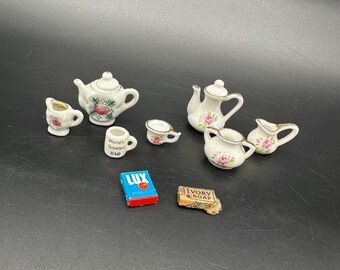 May include: A collection of miniature porcelain tea set pieces, including teapots, creamers, and cups, decorated with pink roses. Also includes a small mug with "World's Greatest Dad" text, a Lux soap box, and a bar of Ivory Soap.