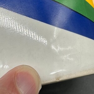 May include: A white ceramic bowl with a rainbow design. The bowl has a blue, green, yellow, and orange stripe pattern.