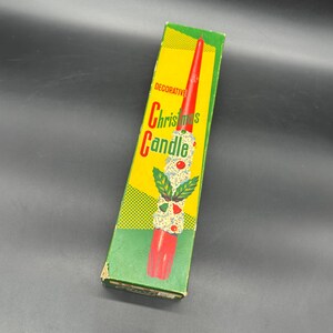 May include: A decorative Christmas candle in a rectangular box. The candle is red with white and green accents, and the box is yellow and green with the words "Decorative Christmas Candle".