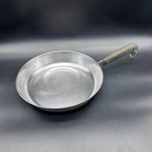 Puede incluir: Una taza de cerámica blanca con asa negra y el texto "But First, Coffee" en negrita negra. La taza se encuentra sobre un fondo borroso, sugiriendo un ambiente acogedor.