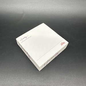 May include: A white rectangular box with the word "Humalog" in a handwritten font on the sides and top. The word "Lilly" is printed in red on the side. The box is on a dark surface.