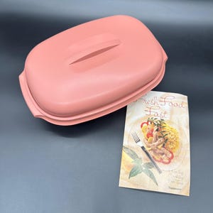 Puede incluir: Un recipiente rosa rectangular para guardar alimentos con asa en la tapa. Un folleto con el texto "Fresh Food Fast" y una imagen de comida está junto al recipiente.