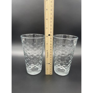 May include: Two clear glass tumblers with a textured, bubbled surface. The glasses are approximately 6 inches tall.