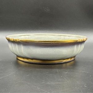 May include: A light blue ceramic bowl with a gold rim and base. The bowl has a fluted design on the sides and a dark brown band just below the gold rim. The bowl is likely for decorative or serving purposes.