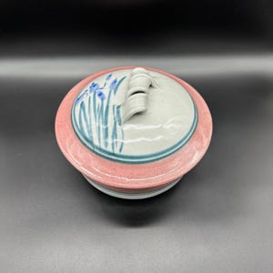 May include: A ceramic lidded dish with a pink rim and a blue and green floral design. The lid has a small handle.
