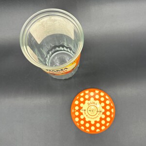 May include: A clear glass jar with a ridged base and a matching orange lid. The lid is decorated with white polka dots and the text "BAMA". The jar has a label with the text "BAMA".