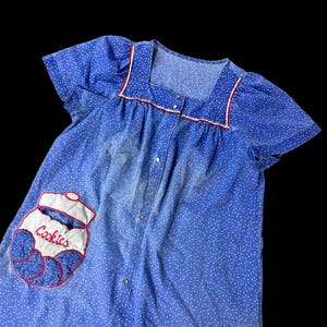 May include: A blue and white polka dot short-sleeved nightgown with a red and white trim around the neckline. The nightgown has a button-up front and a patch pocket with an embroidered cookie jar design that says "Cookies".