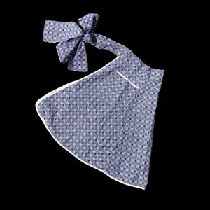 May include: A vintage apron with a matching bow, featuring a repeating pattern of blue and purple floral designs on a gray background. The apron has a white trim and a pocket.