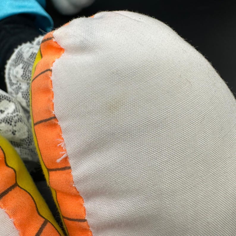 Peut inclure: Gros plan sur un oreiller en tissu blanc avec une bordure orange et jaune. Le tissu a une apparence textur&eacute;e et tiss&eacute;e.