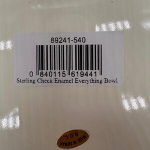 Op de afbeelding: Een wit rechthoekig productlabel met de tekst 89241-540, een streepjescode en de tekst Sterling Check Enamel Everything Bowl. Onder het label bevindt zich een kleine ovale gouden sticker met de tekst MADE IN TAIWAN R.O.C. op een glanzend oppervlak.
