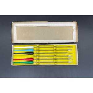 May include: A set of six cocktail forks in a yellow box. The forks have colorful handles in blue, black, red, and green.