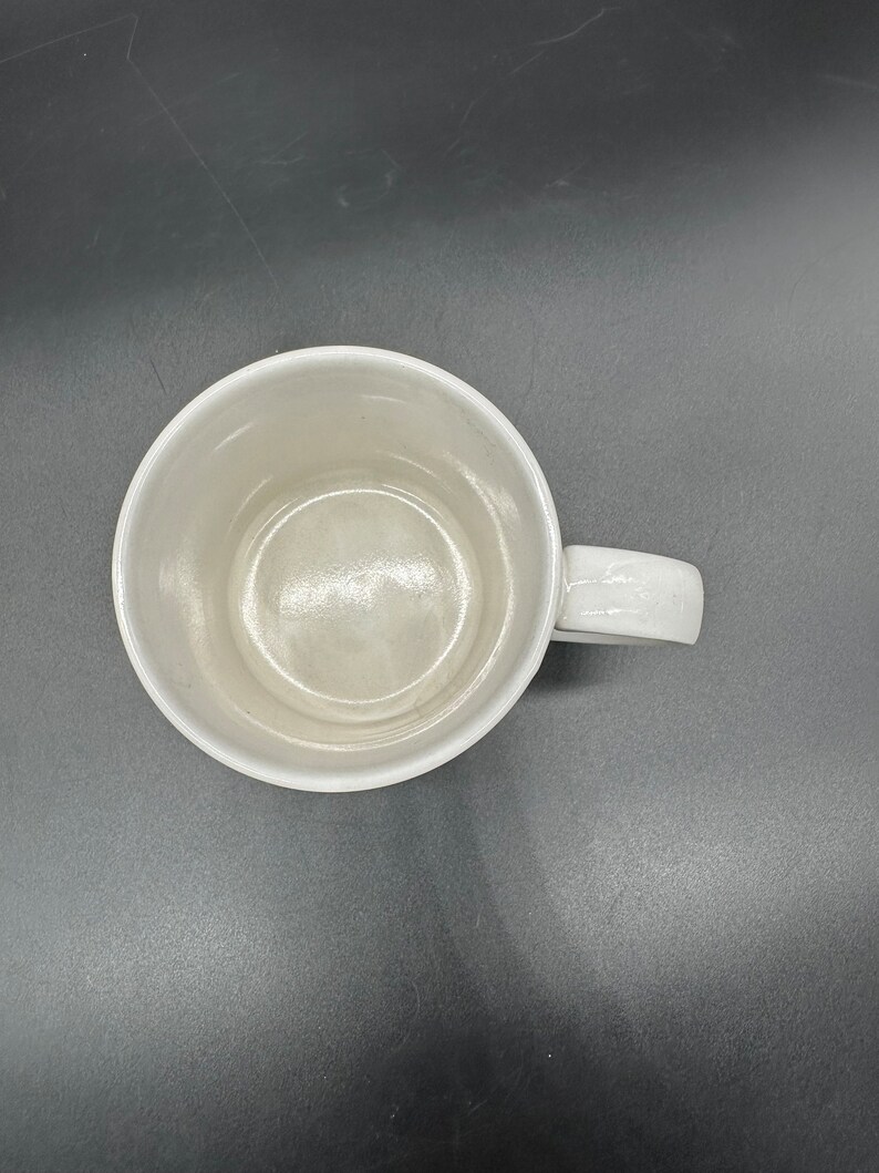 May include: A white ceramic mug with a handle. The mug is empty and has a smooth, glossy finish.